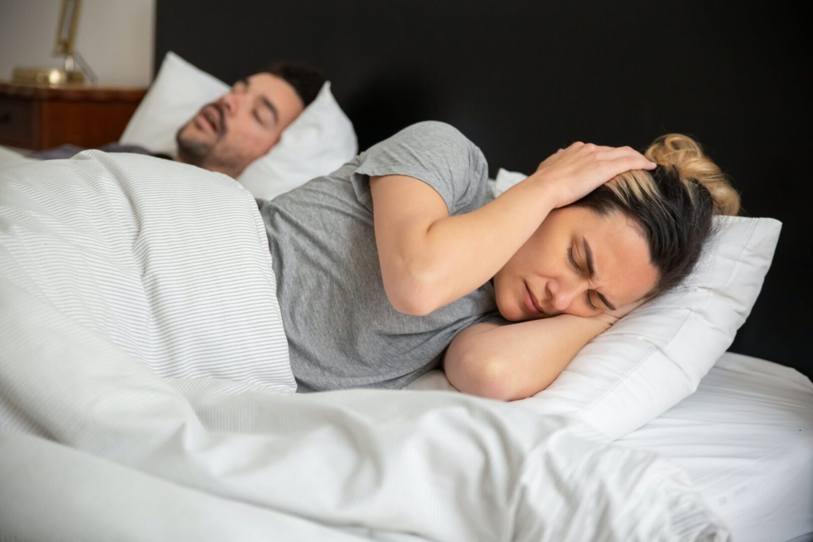 A man and woman sleeping in bed with one of them covering their ears.