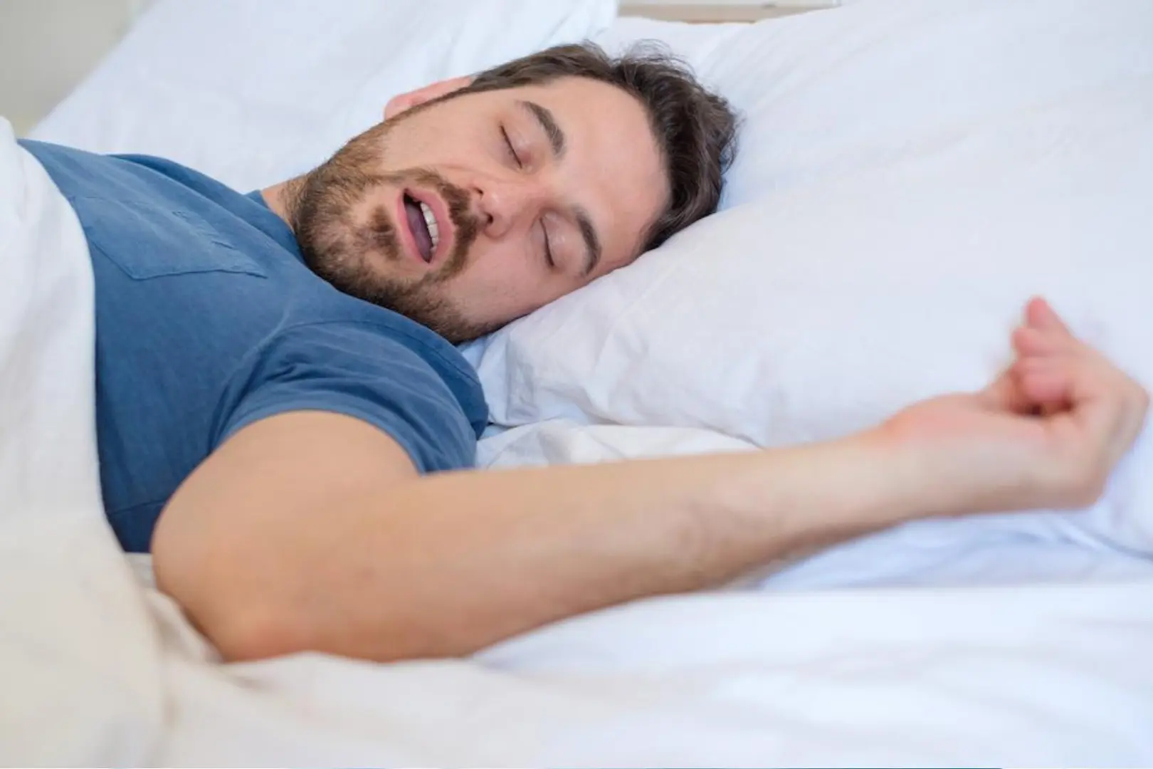 A man sleeping on a white bed wearing a blue tshirt